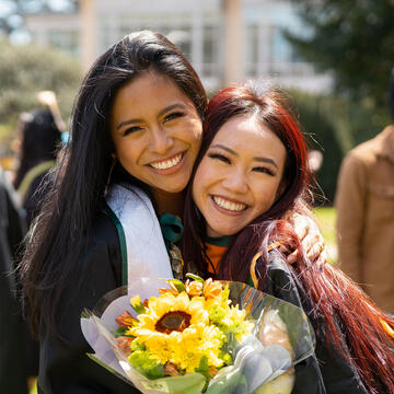 Two graduates pose for photo, holding flowers