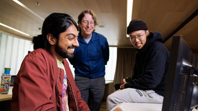 Three people look at a computer