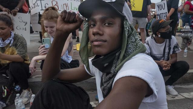 African American man sits in protest with fist raised