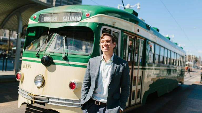 Student stands near an antique street car.