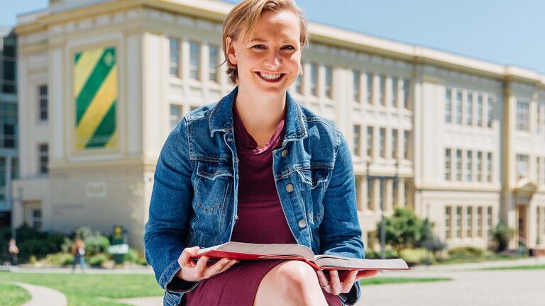 Student sitting in the sun with a book.