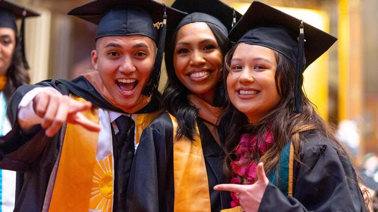 Three students wearing graduation regalia pose for a picture in Saint Ignatius church