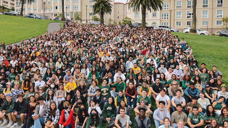 New Fall 2022 students sit for a group portrait on a grassy hill.