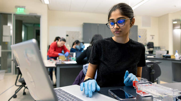 Student enters information into a laptop while working in a science lab.