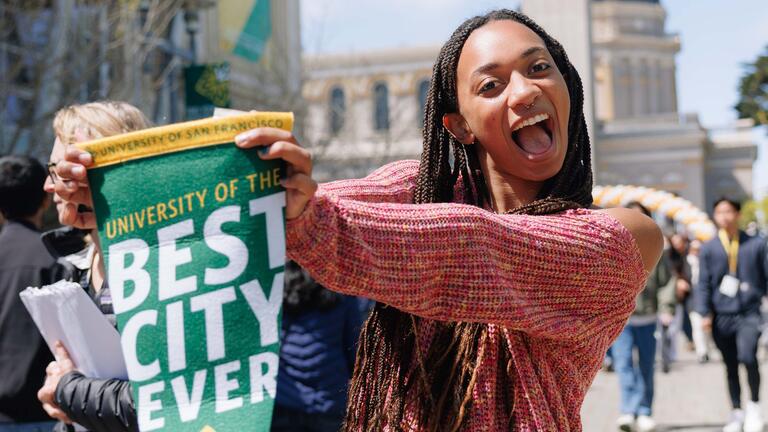 Student holding a flag that says "University of the Best City Ever"