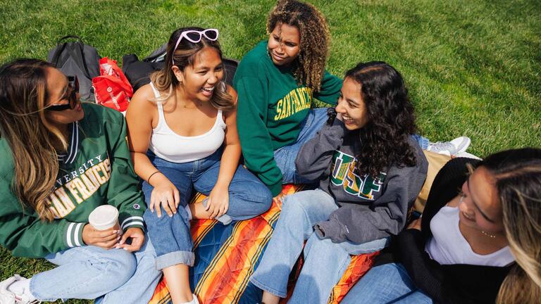 USF alumni sitting on the ground and smiling