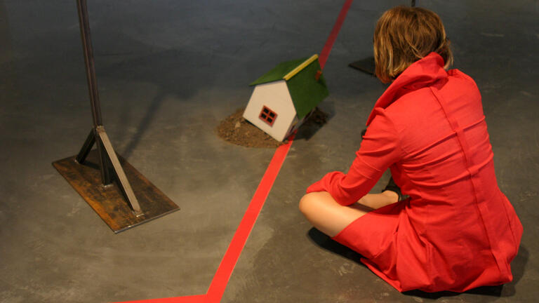 Person in red dress sitting near a miniature house