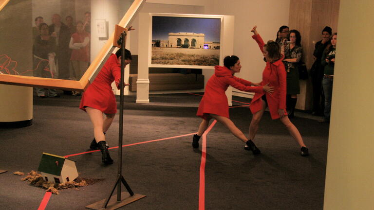 Performers in red dresses interacting in an art gallery