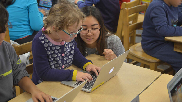 teacher uses laptop with elementary school student