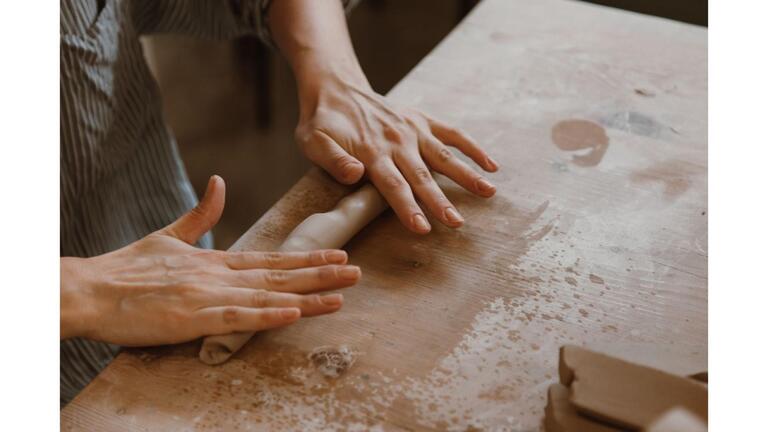 Hands rolling clay out on a table 