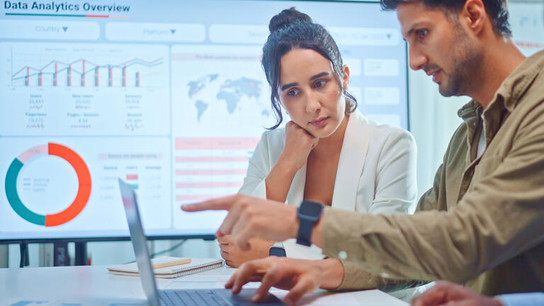 Two data analysts look at a computer screen