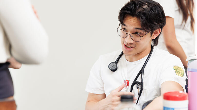 Nursing student with stethoscope talking to event attendee during a campus health fair