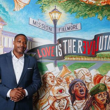 Director stands in front of a mural that reads "Love is the Revolution"