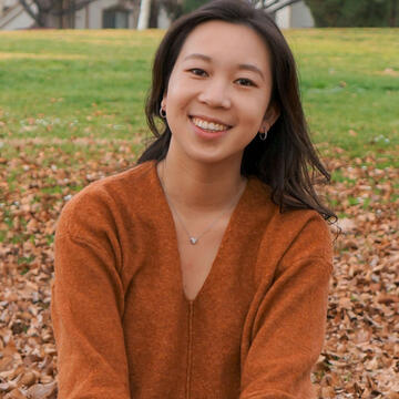 Student sits on a pile of leaves and smiles.