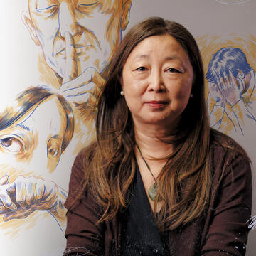 Eileen Fung sits in front of a mural with faces on it.