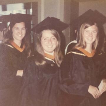 Three alumni dressed in their graduation gowns.