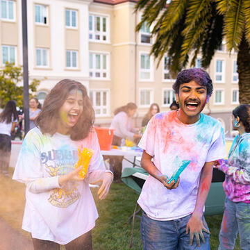 two students throwing powder dye in the air to celebrate the holi festival