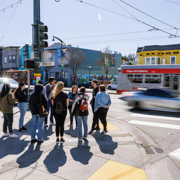 Group of students standing on the sidewalk next to busy street