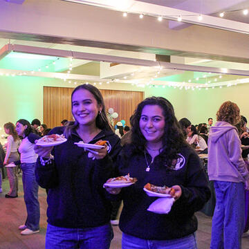 Two students posing with pizza at an event