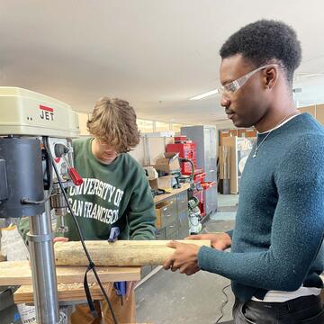 two students making a wooden pole in woodshop