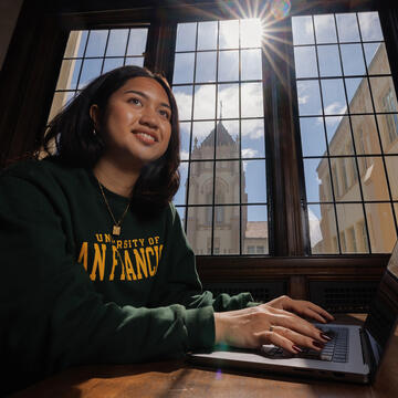 Student types on a laptop in front of a large window