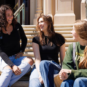 Three students talk and laugh on staircase.