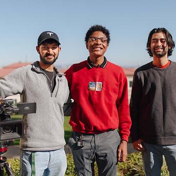 Students posing outdoors with a film camera