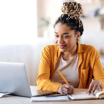 Young professional taking notes and looking at laptop