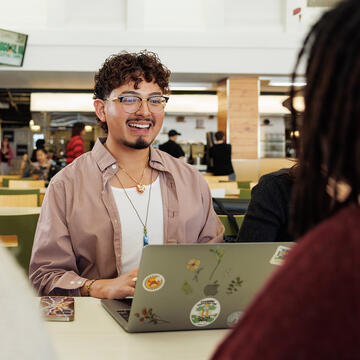 USF student working on laptop in cafeteria, smiling
