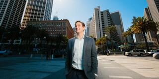 Student walks down the street with SF skyline behind him.