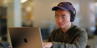 Student with headphones on studies on a laptop.